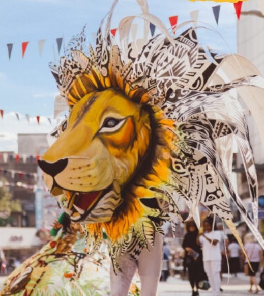 Photo- headshot of a person in a lion costume with long feathers as a mane.