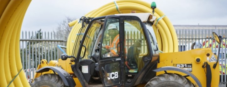 Photo of a JCB with a driver sitting in the cab with an orange visi jacket and white hard hat