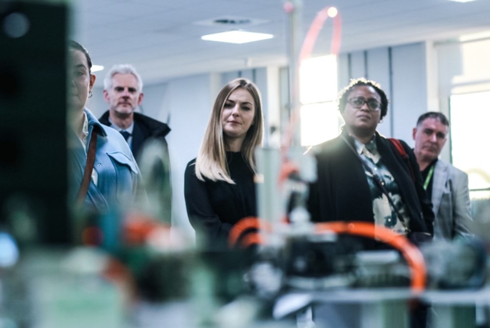 5 people, 3 ladies and 2 men in a Institute of technology classroom looking at digital technology equipment.